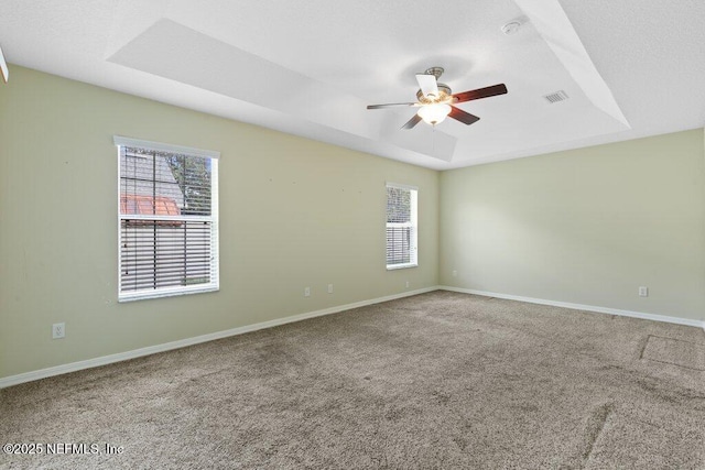 empty room featuring a tray ceiling, a ceiling fan, plenty of natural light, and carpet