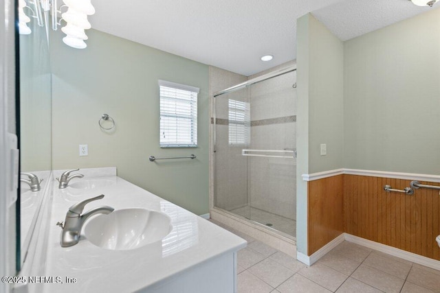 bathroom with a stall shower, double vanity, tile patterned floors, a wainscoted wall, and a textured ceiling