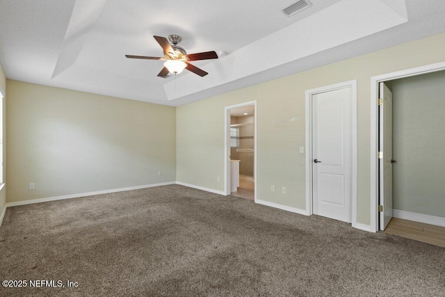 unfurnished bedroom with carpet floors, a tray ceiling, connected bathroom, baseboards, and ceiling fan