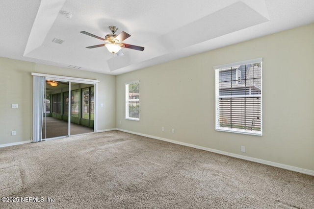 carpeted spare room with a raised ceiling, ceiling fan, and baseboards