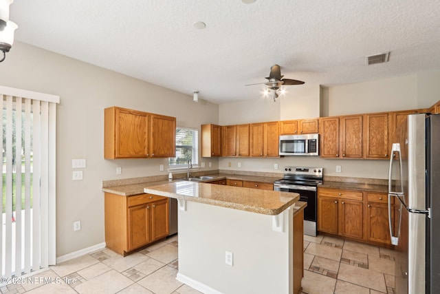 2454 Woodstork Ct, Saint Augustine, FL 32092 - kitchen featuring appliances with stainless steel finishes, a kitchen island, ceiling fan, brown cabinets, and light countertops