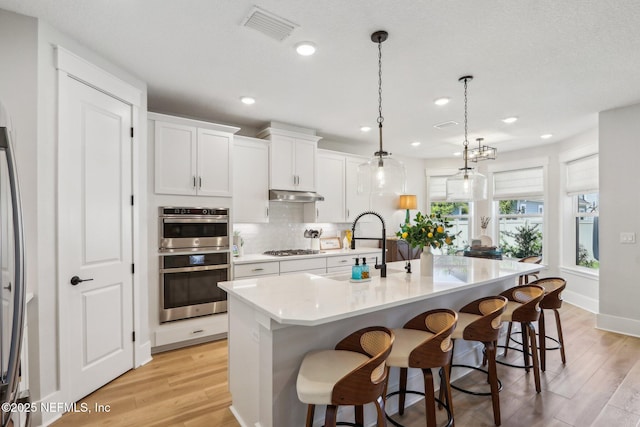 102 Blue Oak Ct, Ponte Vedra, FL 32081 - kitchen with under cabinet range hood, appliances with stainless steel finishes, decorative backsplash, light wood-style floors, and recessed lighting
