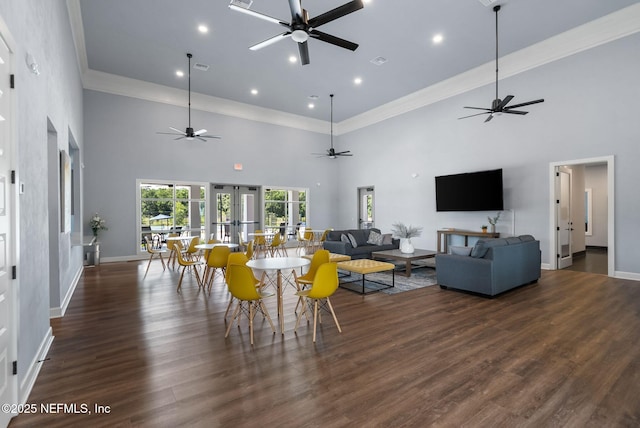 dining area with a towering ceiling, ceiling fan, baseboards, wood finished floors, and crown molding
