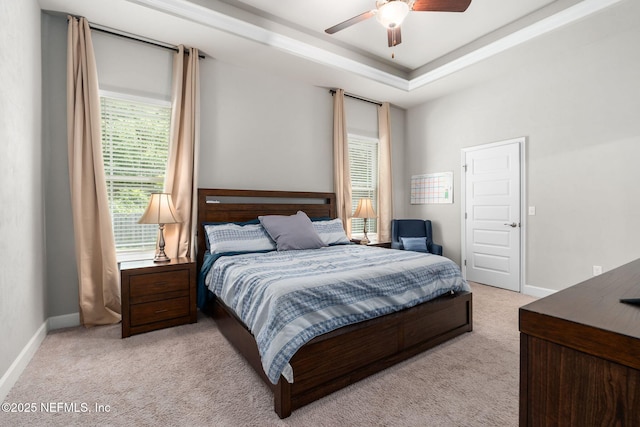 bedroom featuring light carpet, baseboards, a tray ceiling, and a ceiling fan
