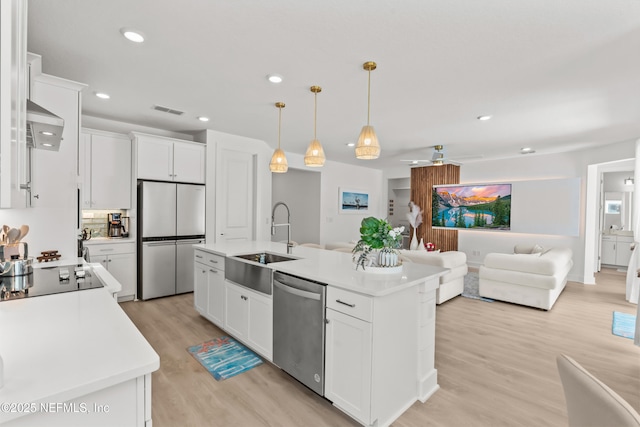 kitchen with stainless steel appliances, a sink, light wood-style flooring, open floor plan, and light countertops