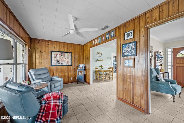 sitting room with wooden walls, ceiling fan, crown molding, light tile patterned flooring, and baseboards