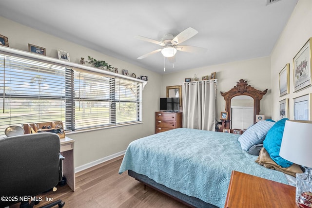 bedroom with wood finished floors, baseboards, an office area, and a ceiling fan