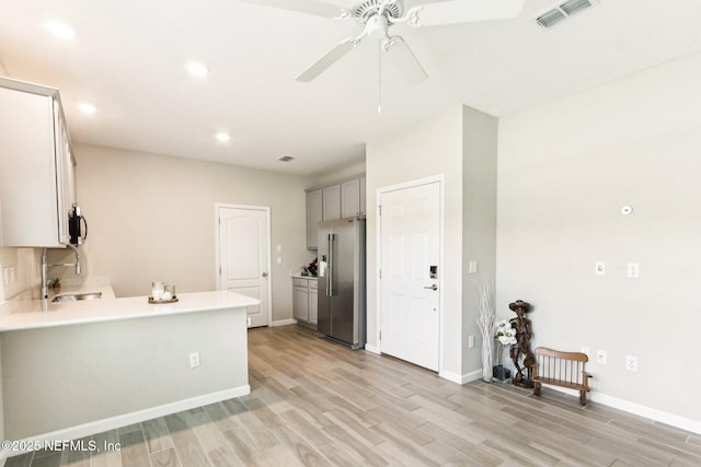 kitchen with appliances with stainless steel finishes, a sink, gray cabinetry, light wood finished floors, and light countertops