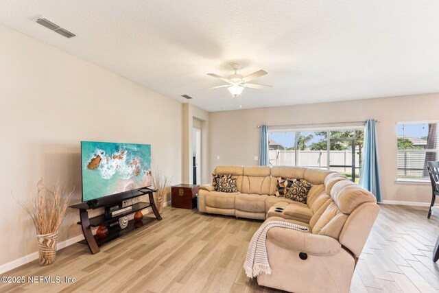 living area featuring light wood finished floors, baseboards, and ceiling fan