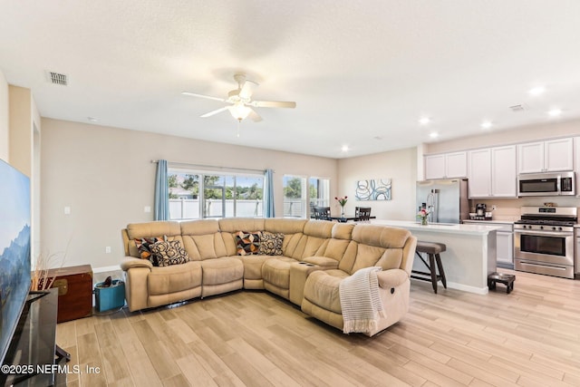 living room featuring light wood-style flooring, a ceiling fan, and recessed lighting