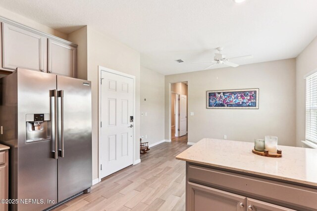 kitchen with stainless steel fridge, a ceiling fan, light wood-style floors, baseboards, and light stone counters