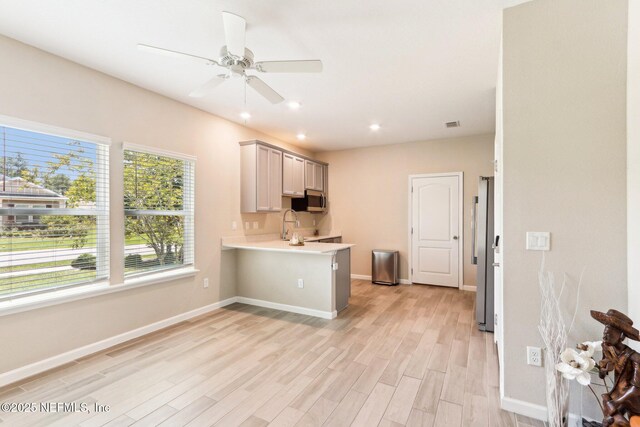 kitchen with stainless steel appliances, light wood-style flooring, light countertops, a ceiling fan, and a peninsula
