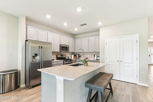 kitchen with appliances with stainless steel finishes, a sink, light wood-style flooring, recessed lighting, and light stone countertops