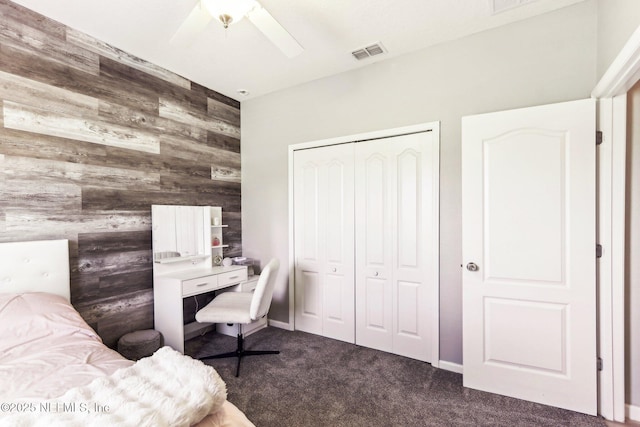 bedroom with wood walls, dark colored carpet, a closet, an accent wall, and a ceiling fan