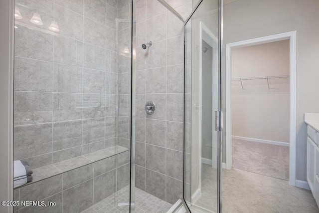 full bath featuring a shower stall, vanity, a walk in closet, and baseboards