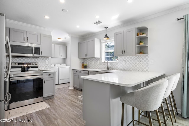 kitchen featuring appliances with stainless steel finishes, washing machine and dryer, gray cabinets, a peninsula, and crown molding