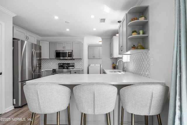 kitchen featuring stainless steel appliances, washer / clothes dryer, a peninsula, a sink, and light countertops