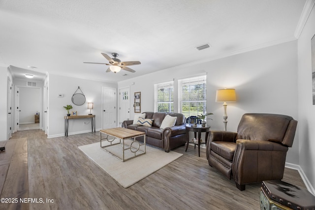 living area with wood finished floors, ceiling fan, crown molding, and baseboards