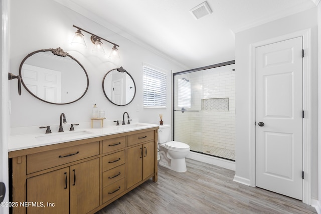 bathroom featuring a stall shower, double vanity, toilet, ornamental molding, and wood finished floors