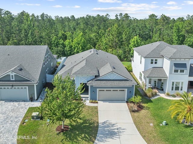 view of front facade with driveway, an attached garage, a front lawn, a view of trees, and a shingled roof