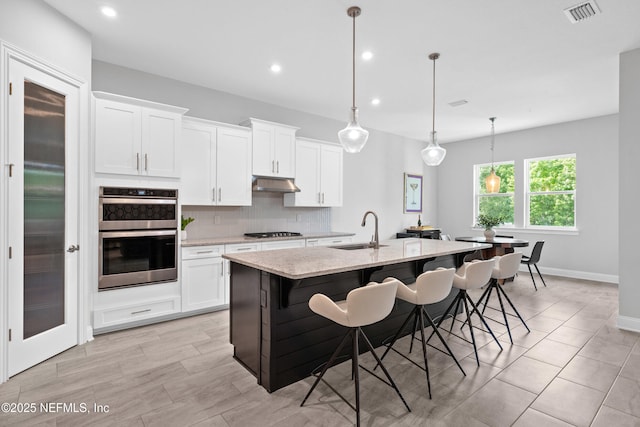 kitchen with a sink, under cabinet range hood, appliances with stainless steel finishes, tasteful backsplash, and light stone counters