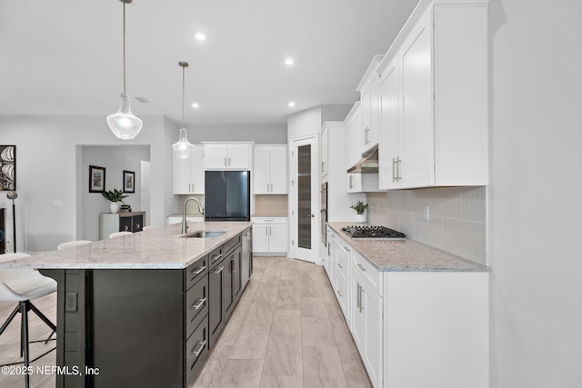 kitchen with black fridge, a sink, under cabinet range hood, stainless steel gas stovetop, and white cabinetry