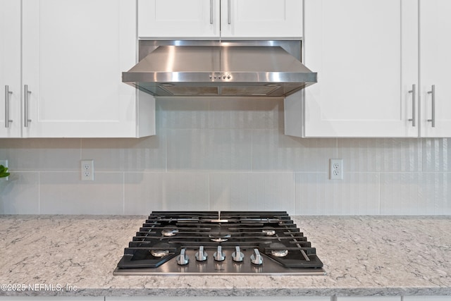 kitchen view of exhaust hood, stainless steel gas cooktop, white cabinetry, and decorative backsplash
