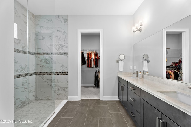 full bath with a marble finish shower, double vanity, and baseboards