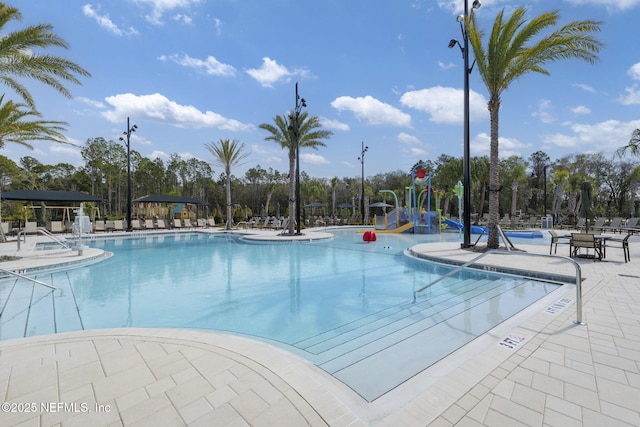 community pool featuring a water slide, a patio area, and view of scattered trees