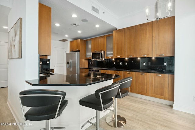 kitchen featuring appliances with stainless steel finishes, backsplash, light wood-style flooring, dark countertops, and brown cabinets
