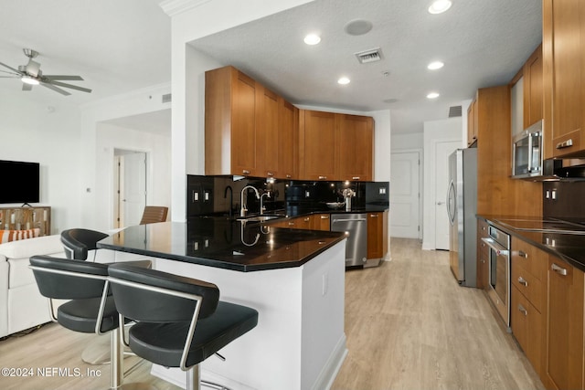 kitchen with appliances with stainless steel finishes, a ceiling fan, a sink, a peninsula, and dark countertops