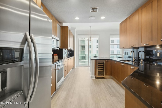 kitchen with stainless steel appliances, wine cooler, a peninsula, light wood finished floors, and brown cabinets