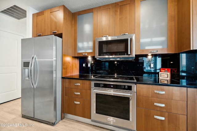 kitchen with appliances with stainless steel finishes, glass insert cabinets, brown cabinetry, and light wood-style flooring