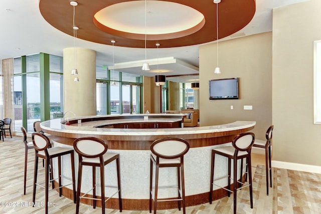 kitchen featuring a tray ceiling, baseboards, a spacious island, decorative light fixtures, and a breakfast bar area