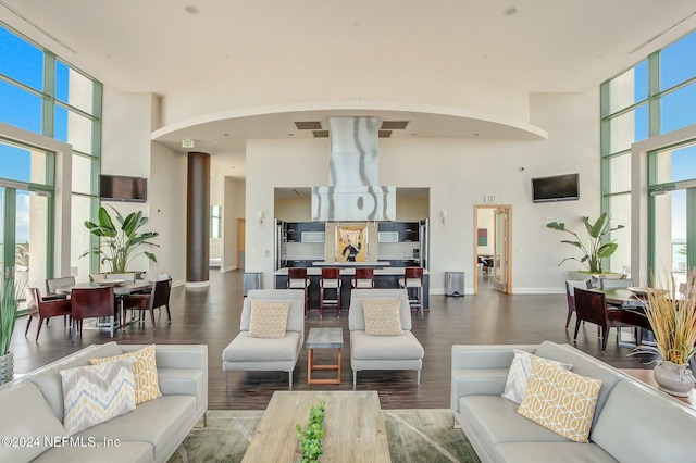 living area with a towering ceiling, arched walkways, wood finished floors, expansive windows, and baseboards
