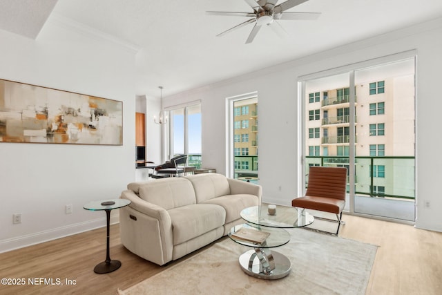 living area featuring wood finished floors, ornamental molding, a ceiling fan, and baseboards