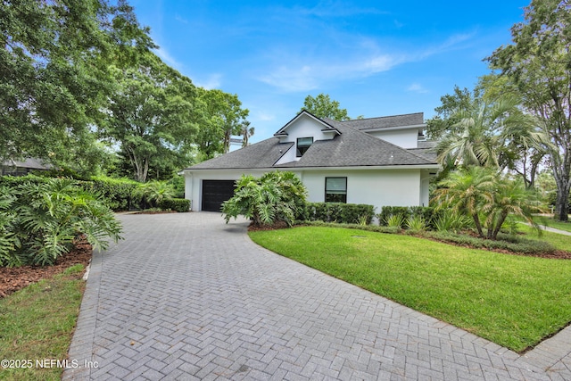 view of front of house featuring stucco siding, an attached garage, decorative driveway, a front yard, and a shingled roof