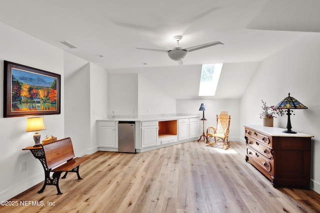 sitting room with a skylight, vaulted ceiling, light wood-style flooring, ceiling fan, and baseboards