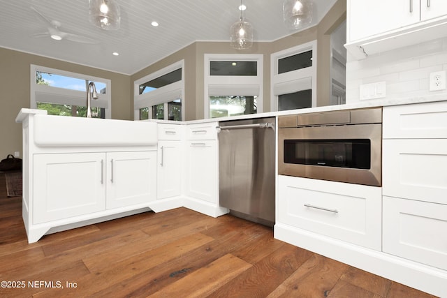 kitchen featuring stainless steel dishwasher, light wood finished floors, white cabinets, pendant lighting, and light countertops
