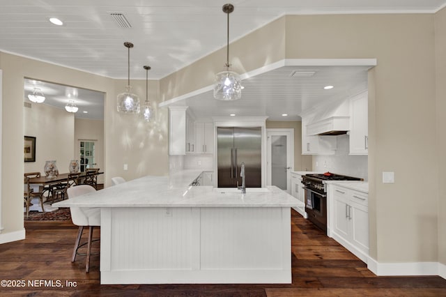 kitchen featuring high end appliances, a peninsula, a sink, tasteful backsplash, and a breakfast bar area