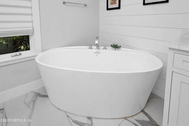 full bath featuring marble look tile flooring, a freestanding tub, and baseboards