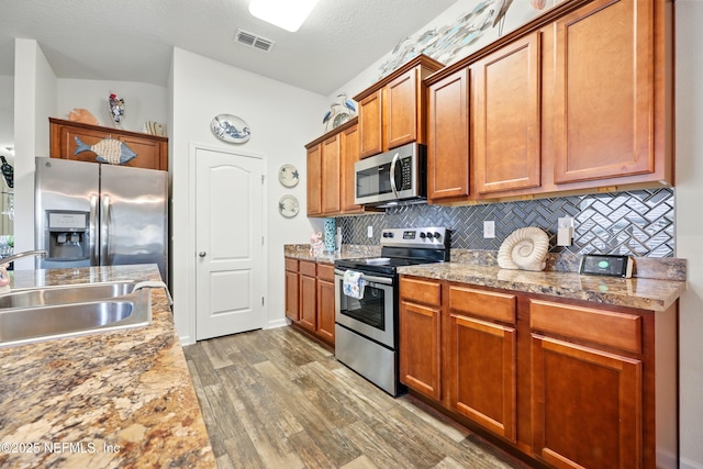 499 Ashby Landing Way, Saint Augustine, FL 32086 - kitchen with appliances with stainless steel finishes, a sink, wood finished floors, backsplash, and brown cabinetry