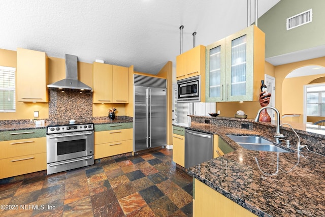 224 Bowles St, Neptune Beach, FL 32266 - kitchen featuring wall chimney range hood, built in appliances, a sink, decorative backsplash, and dark stone countertops