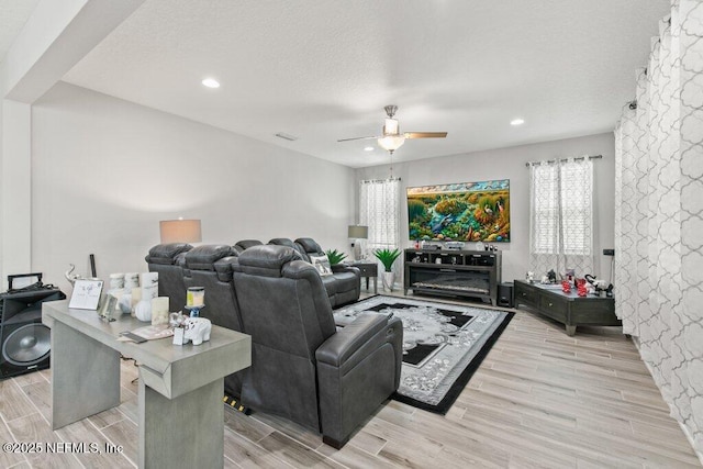 living room featuring ceiling fan, light wood-style floors, a textured ceiling, and recessed lighting