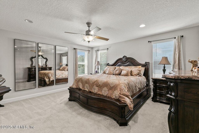 bedroom featuring light colored carpet, multiple windows, a textured ceiling, ceiling fan, and baseboards