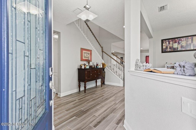 entrance foyer with stairway, light wood-style floors, a textured ceiling, and baseboards