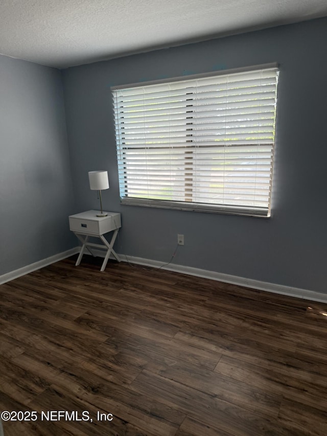 spare room featuring dark wood-style floors and baseboards