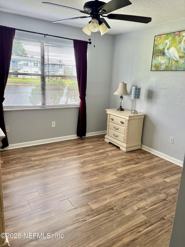 unfurnished bedroom with a textured ceiling, wood finished floors, ceiling fan, and baseboards