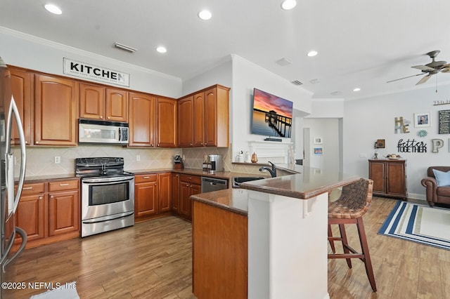 4956 Cypress Links Blvd, Elkton, FL 32033 - kitchen with stainless steel appliances, a peninsula, a kitchen bar, ornamental molding, and light wood-style floors