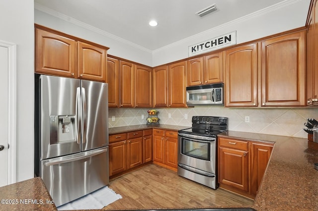 4956 Cypress Links Blvd, Elkton, FL 32033 - kitchen with appliances with stainless steel finishes, brown cabinets, decorative backsplash, ornamental molding, and light wood-style flooring